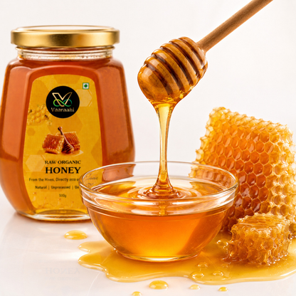 Vaaraahi Raw Honey being poured from a wooden honey dipper into a glass bowl beside honeycomb.